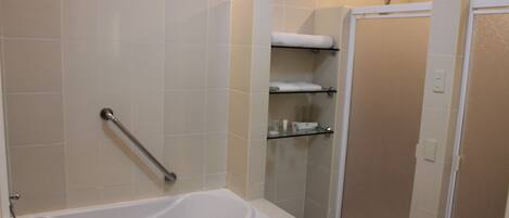 A bathroom with a bathtub, a shower, and a toilet. There is a glass shelf with toiletries.