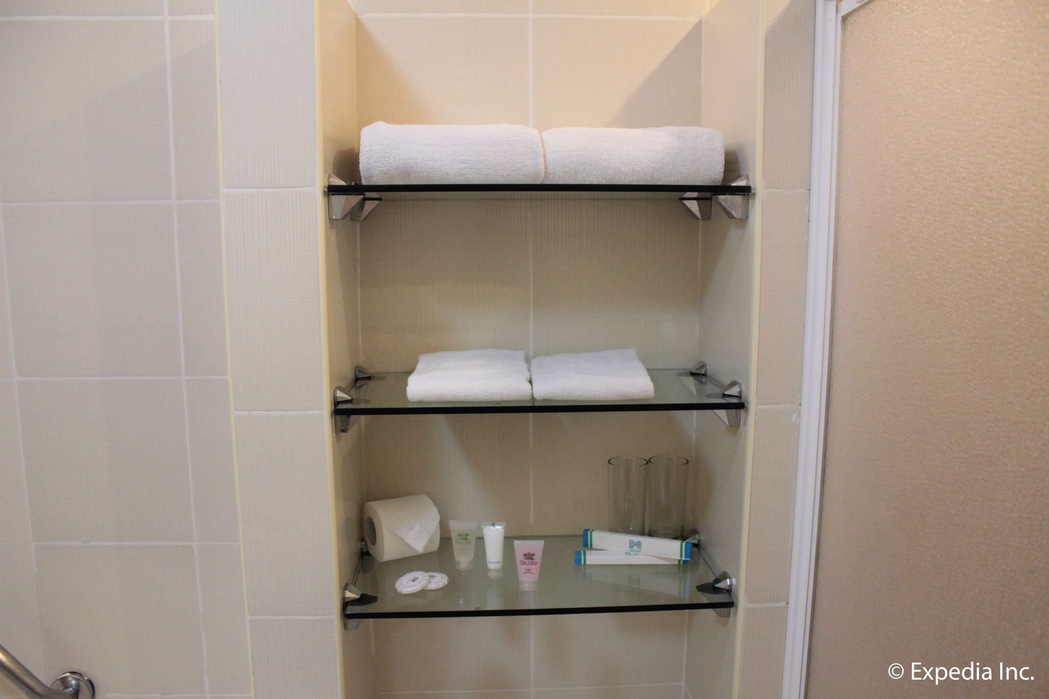 Un baño con tres estantes que sostienen toallas y artículos de aseo.