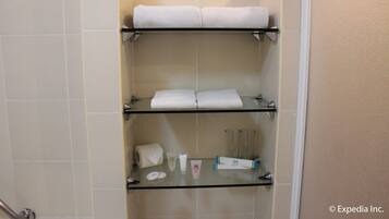 Un baño con tres estantes que sostienen toallas y artículos de aseo.