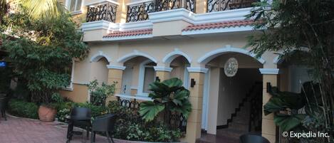 A two-story building with balconies, a covered patio area, and potted plants.
