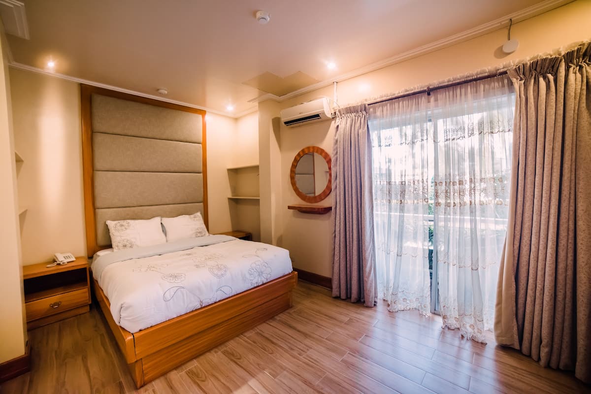 Une chambre à coucher avec un lit en bois, une table de chevet, une commode, un miroir rond et une fenêtre avec des rideaux.