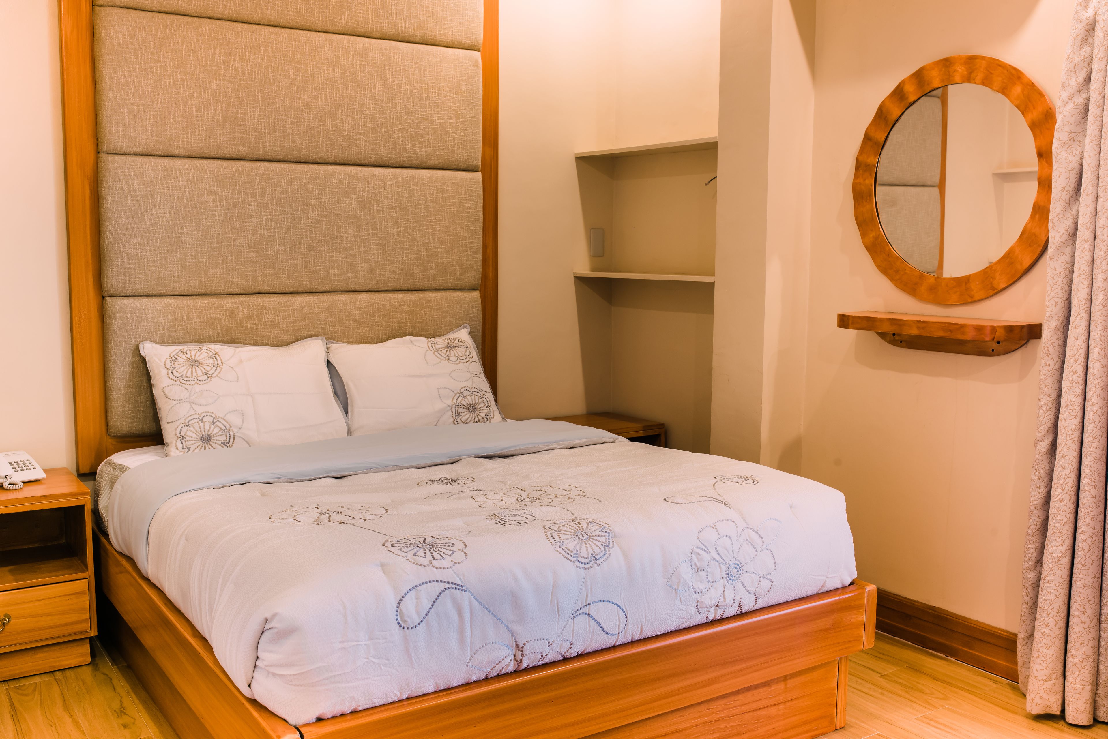 Una cama bien hecha con una colcha estampada con motivos florales, un cabecero de madera y una mesita de noche con una lámpara.