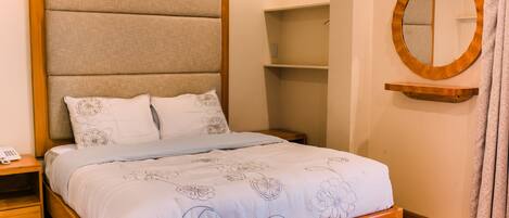 Una cama bien hecha con una colcha estampada con motivos florales, un cabecero de madera y una mesita de noche con una lámpara.