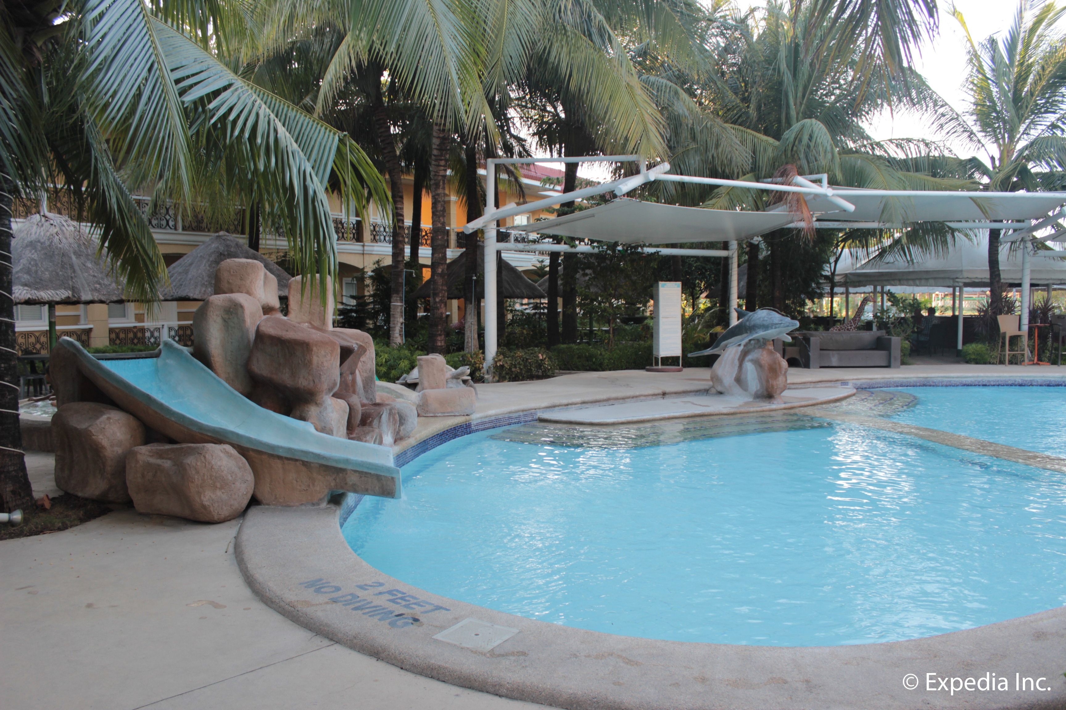 A swimming pool with a slide, palm trees, and a shaded area.
