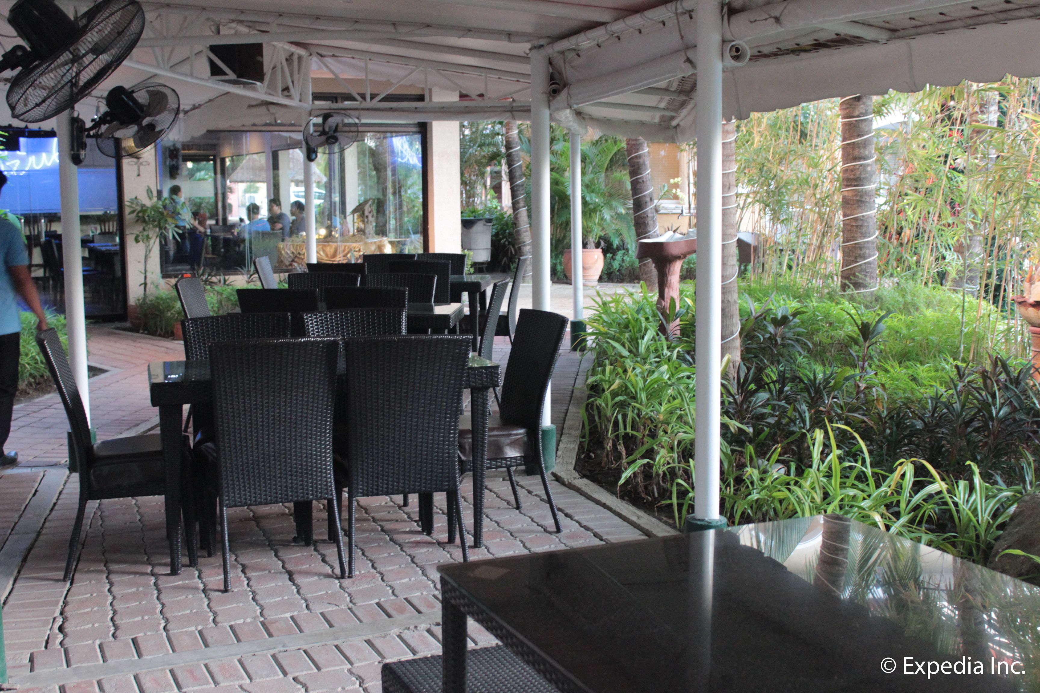 An outdoor patio area with black wicker furniture and a glass table, surrounded by potted plants and a brick floor.