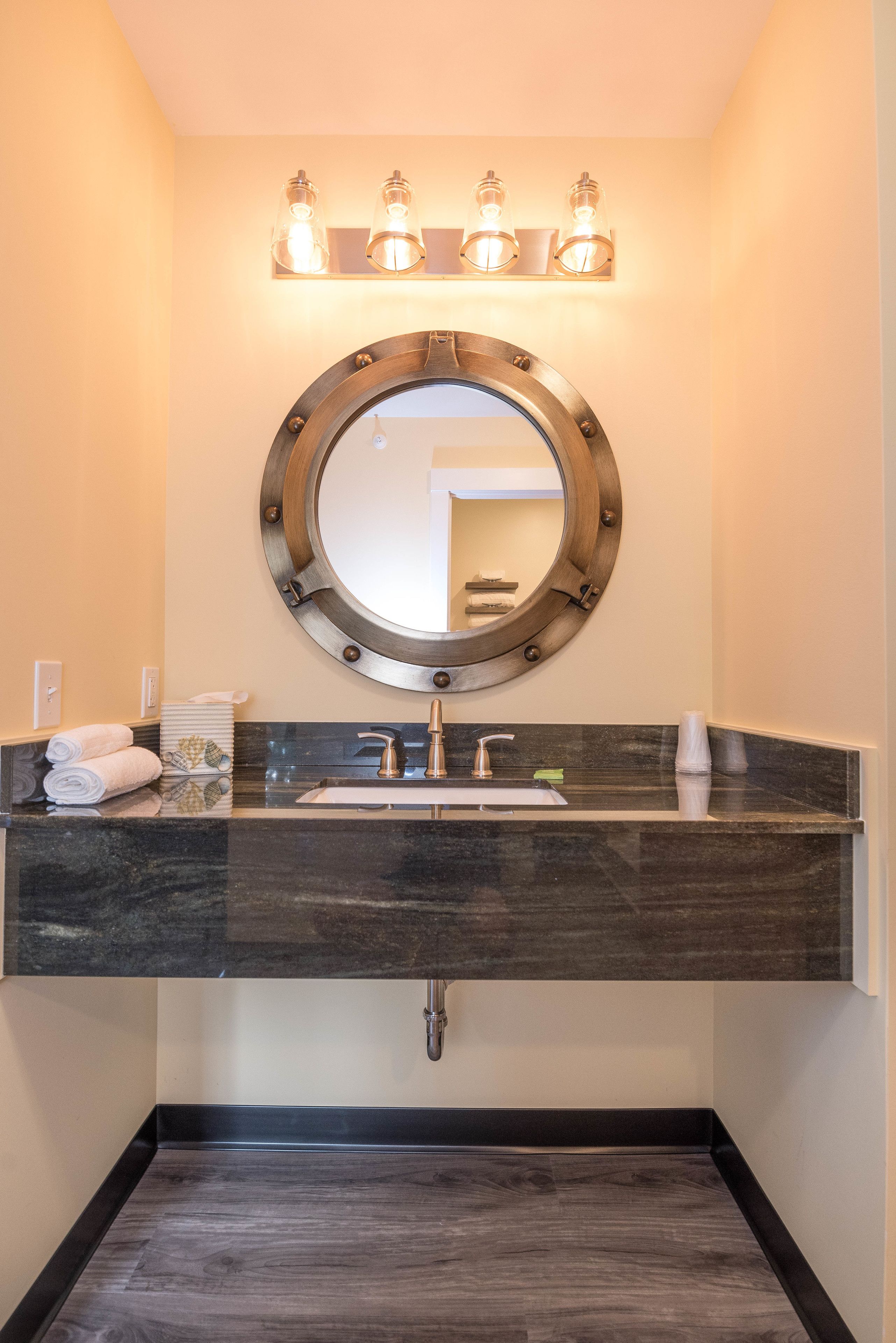 A bathroom with a round mirror, a sink, and a towel rack.