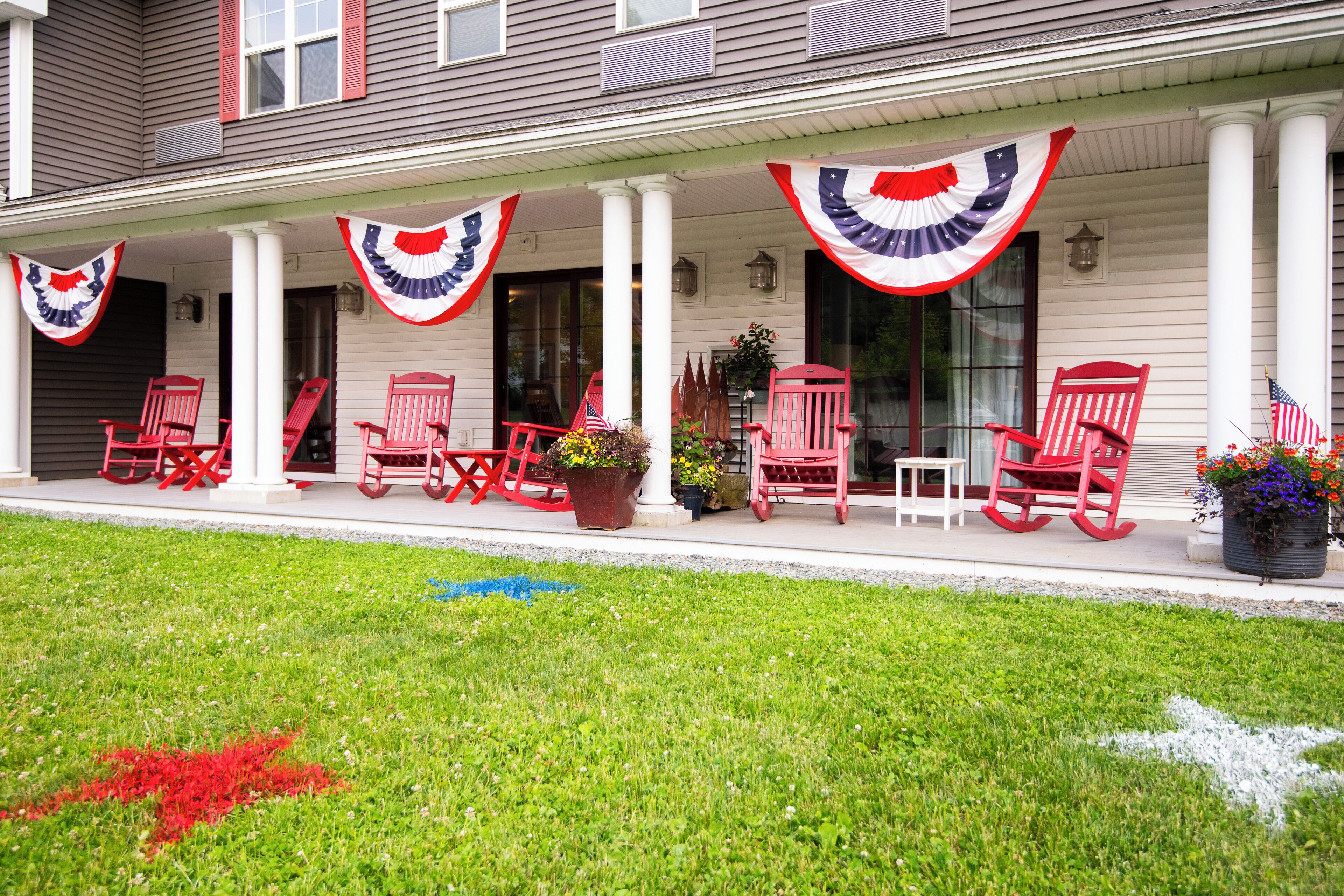 A house with a porch decorated with red, white, and blue bunting, and red rocking chairs.