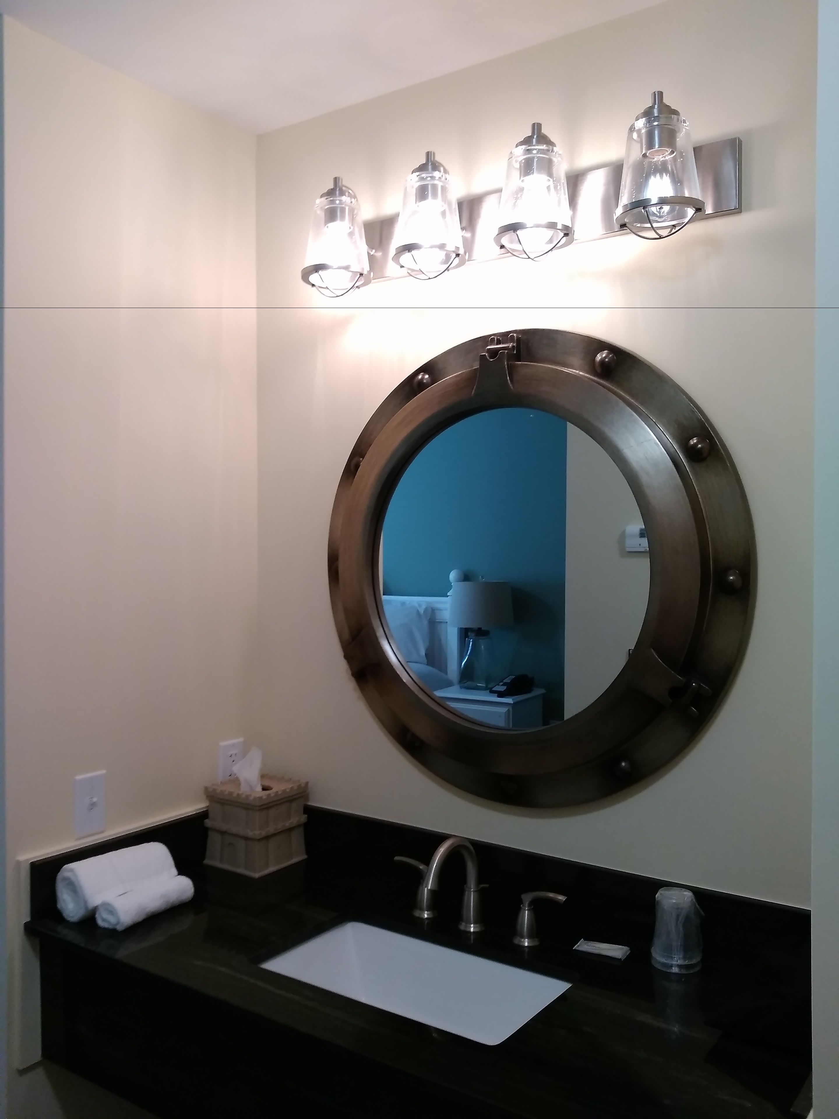 A bathroom with a round mirror, a sink, and three wall-mounted lights.