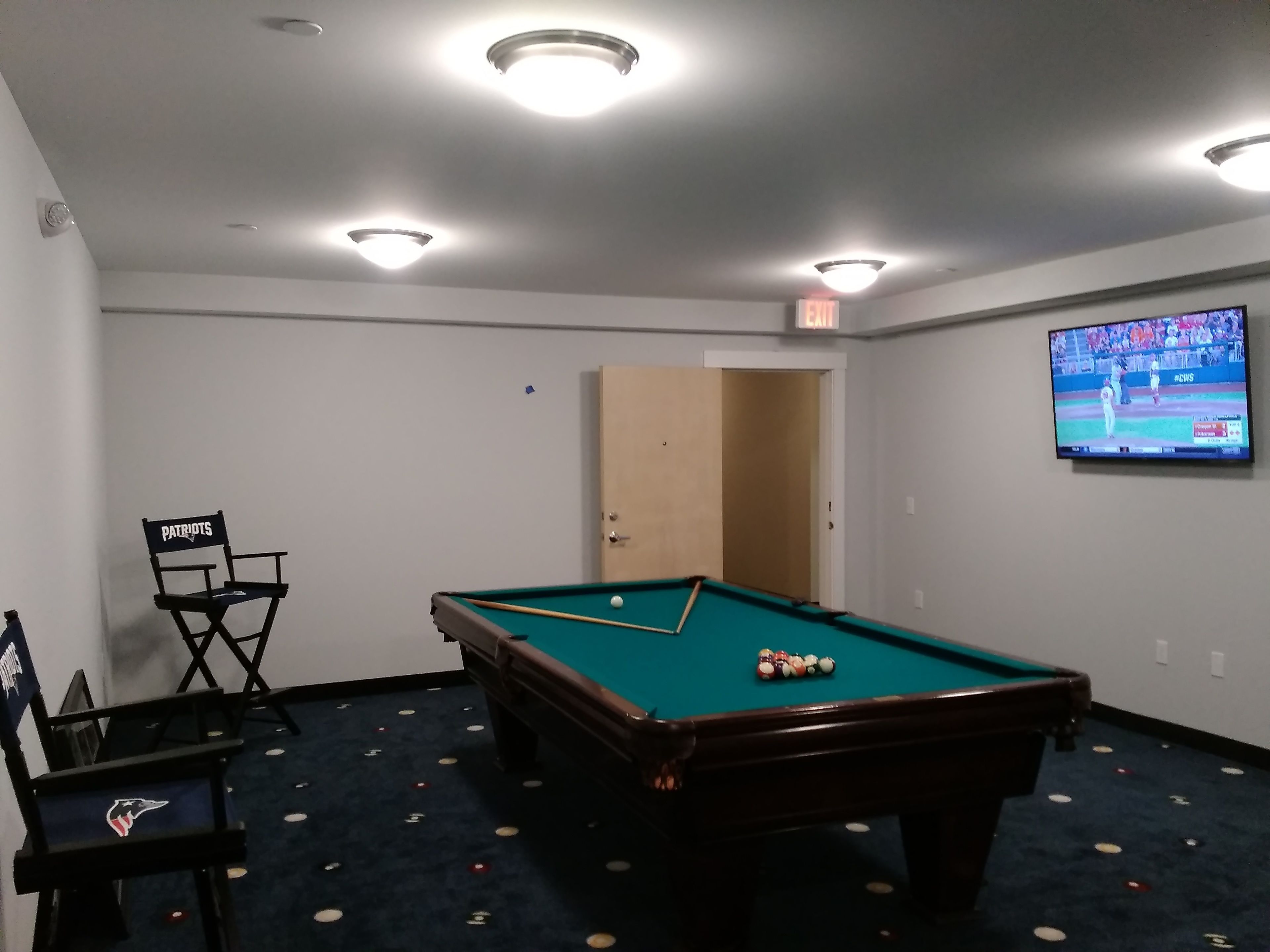 A room with a pool table, a television, and seating with team logos.