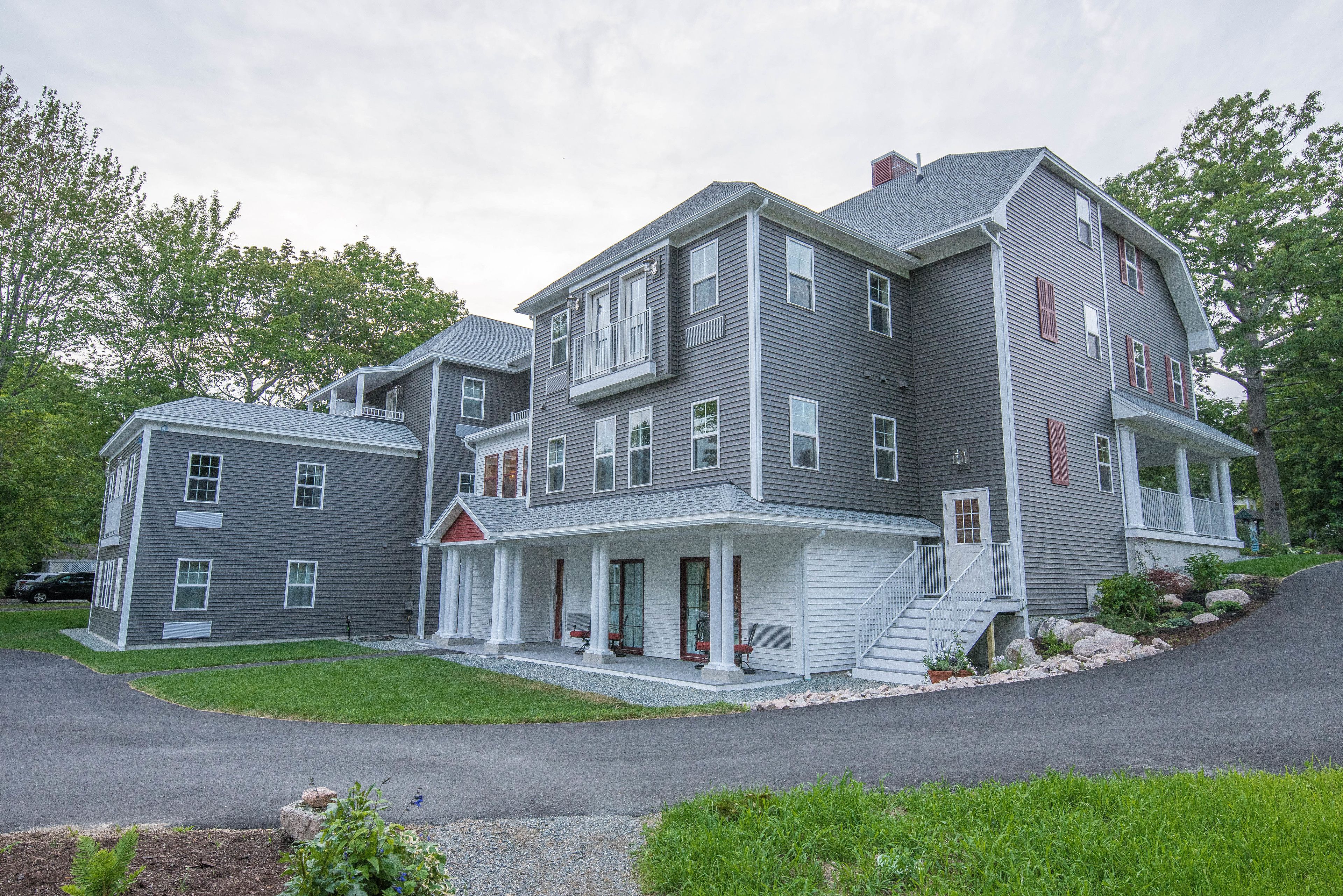 A multi-story residential building with a covered front porch, a small front yard, and a driveway.
