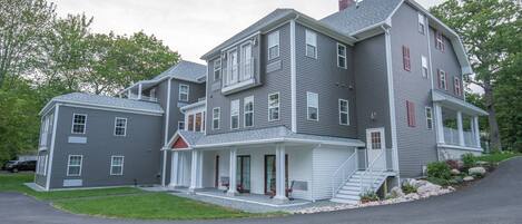 A multi-story residential building with a covered front porch, a small front yard, and a driveway.