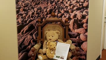 A room with a large scenic poster of a rocky beach and a wooden chair with a teddy bear and a document.