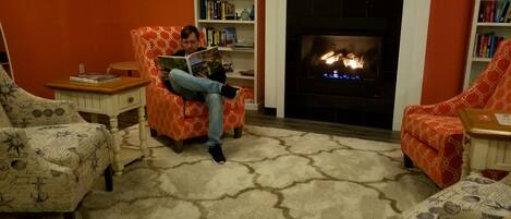 A cozy living room with a fireplace, patterned armchairs, and a bookshelf.