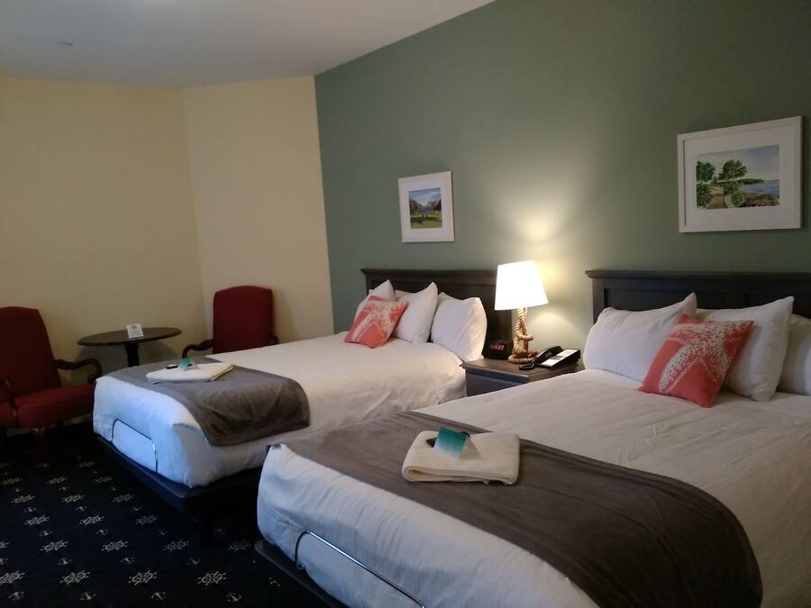 A hotel room with two beds, a red chair, a small table, and a lamp.