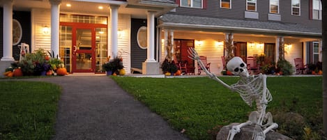 Une maison avec un porche à l’avant, un chemin menant à l’entrée et une décoration représentant un squelette placée sur un rocher.
