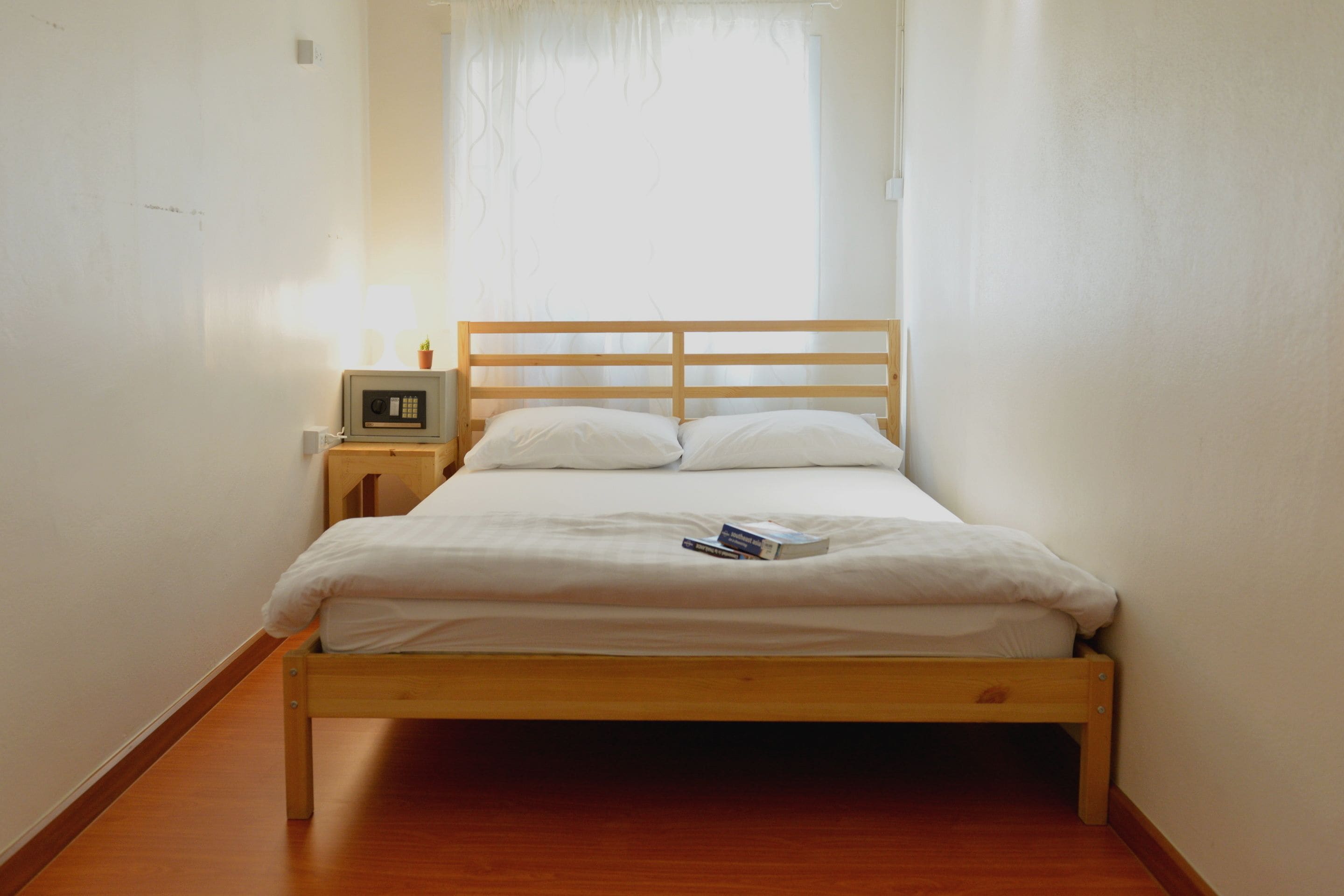 A small, narrow room with a single bed, a bedside table, and a window with curtains.