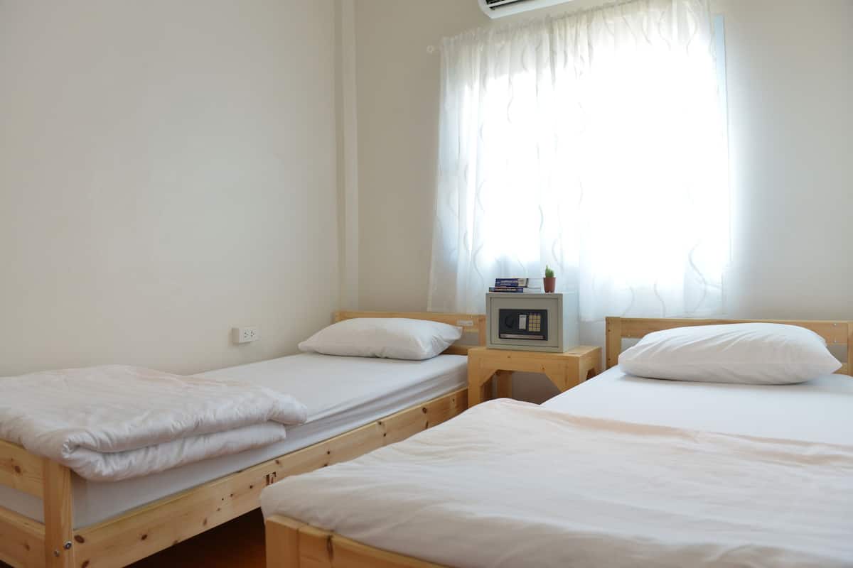 A room with three wooden beds, each with white bedding and pillows. There is a small table with a microwave and a few books.