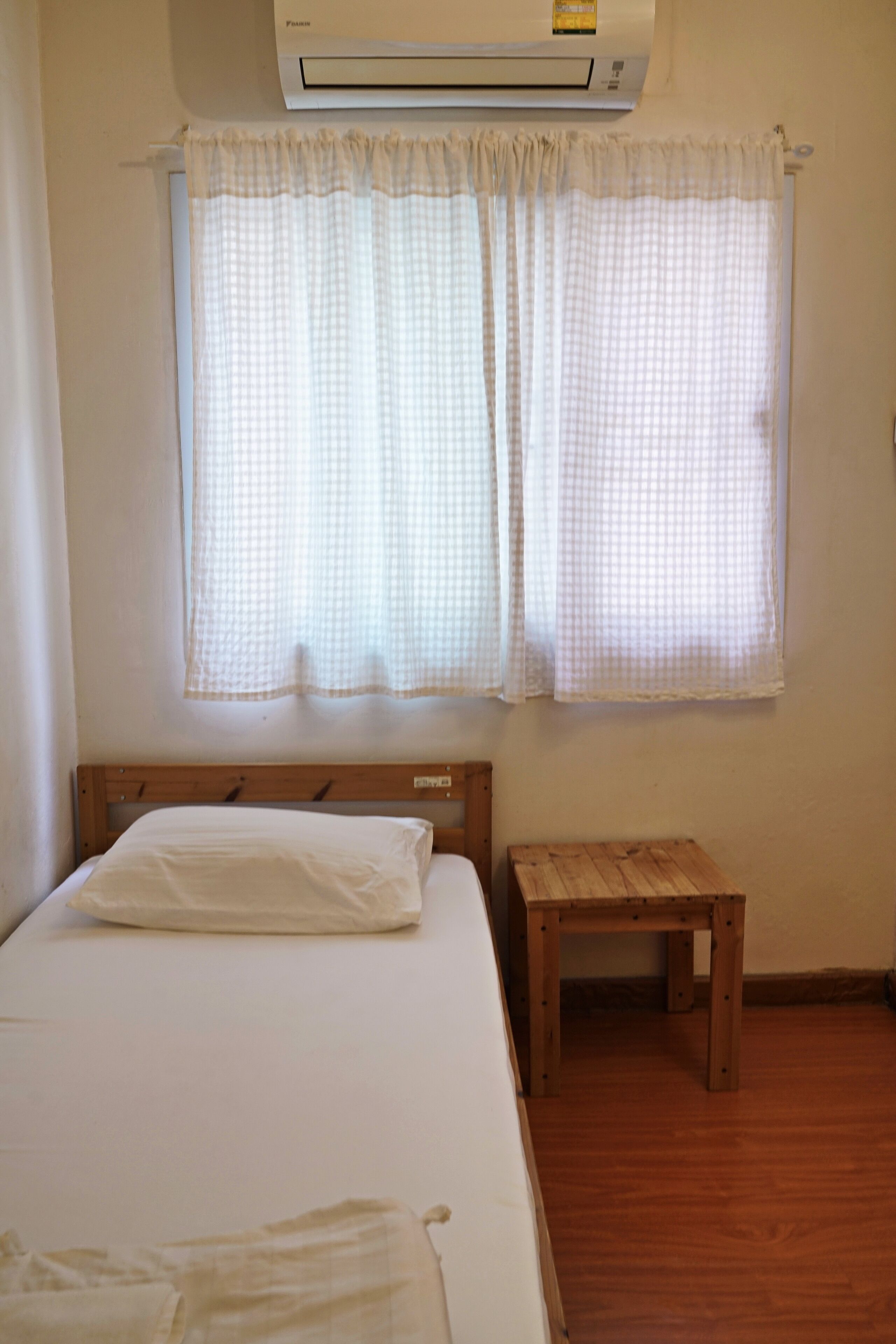 A bedroom with a bed, a wooden nightstand, a window with curtains, and an air conditioning unit.