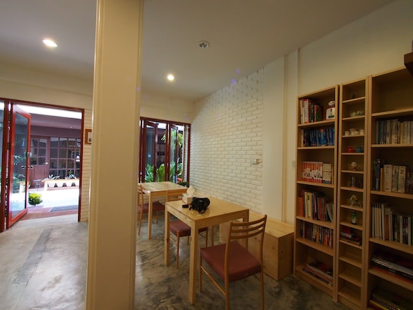 A room with a dining table and chairs, a bookshelf, and a white brick wall.