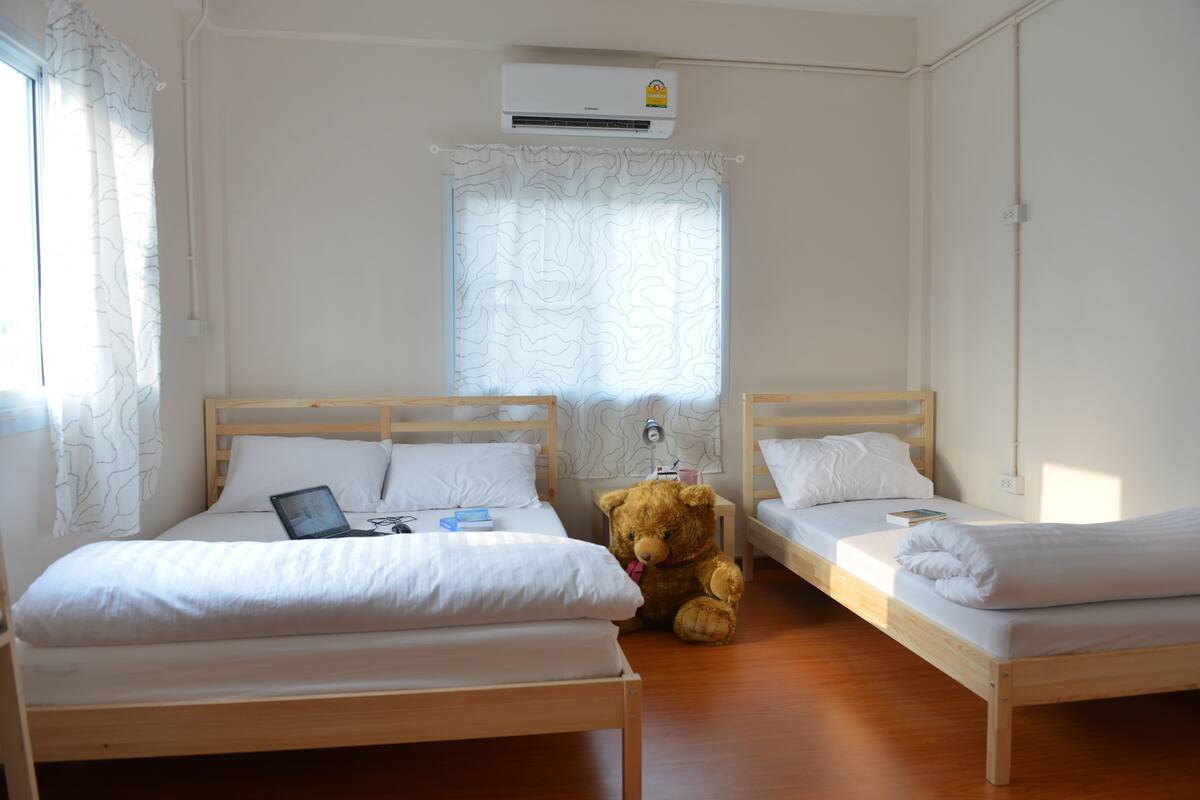 A room with two wooden beds, a teddy bear, and an air conditioning unit.