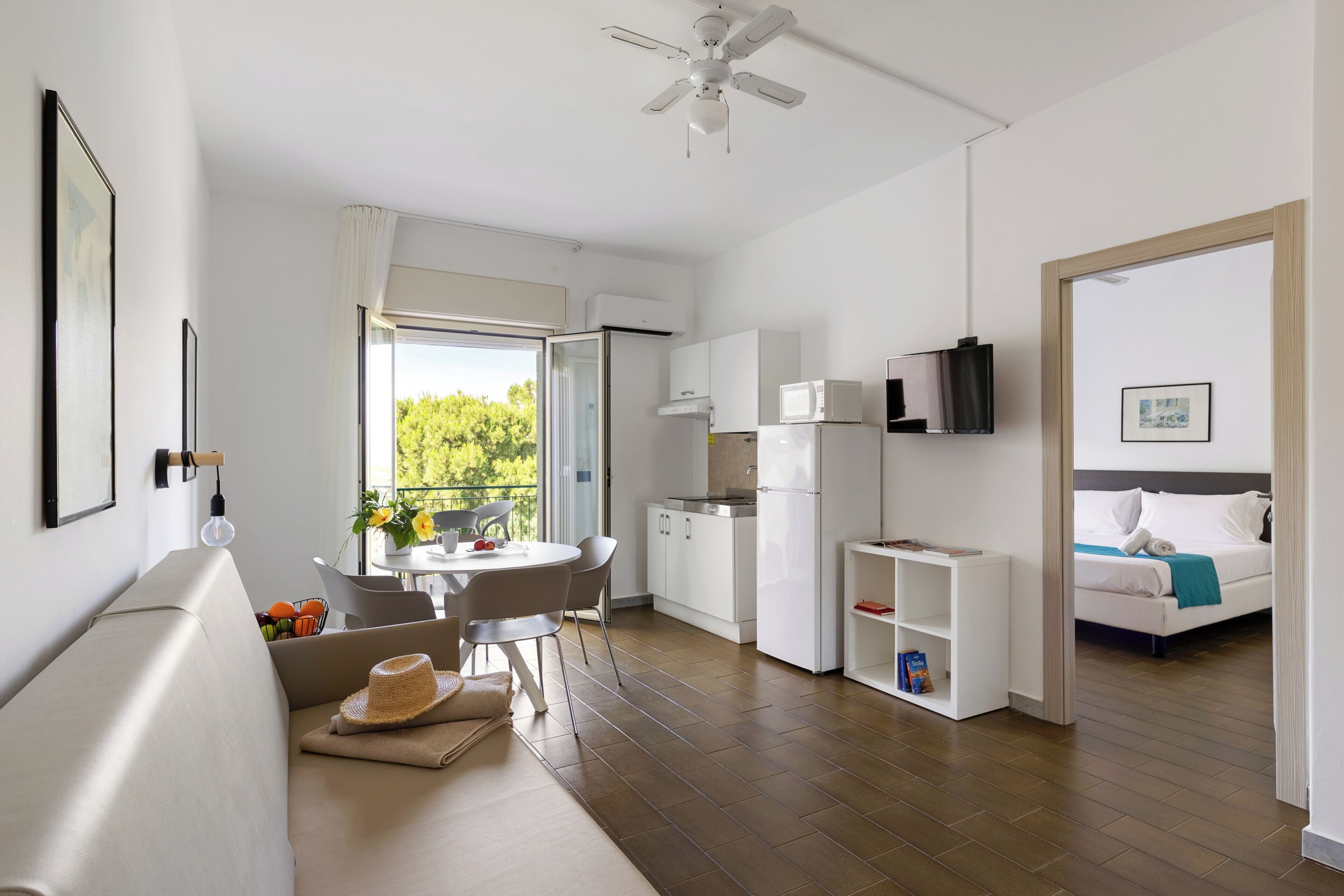 A modern, well-lit room with a sofa, dining table, and kitchenette.
