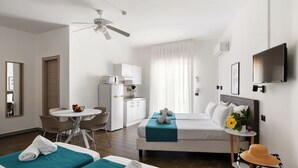 A hotel room with two beds, a desk, a chair, a TV, and a ceiling fan. - Villa Collina (Giardini Naxos)