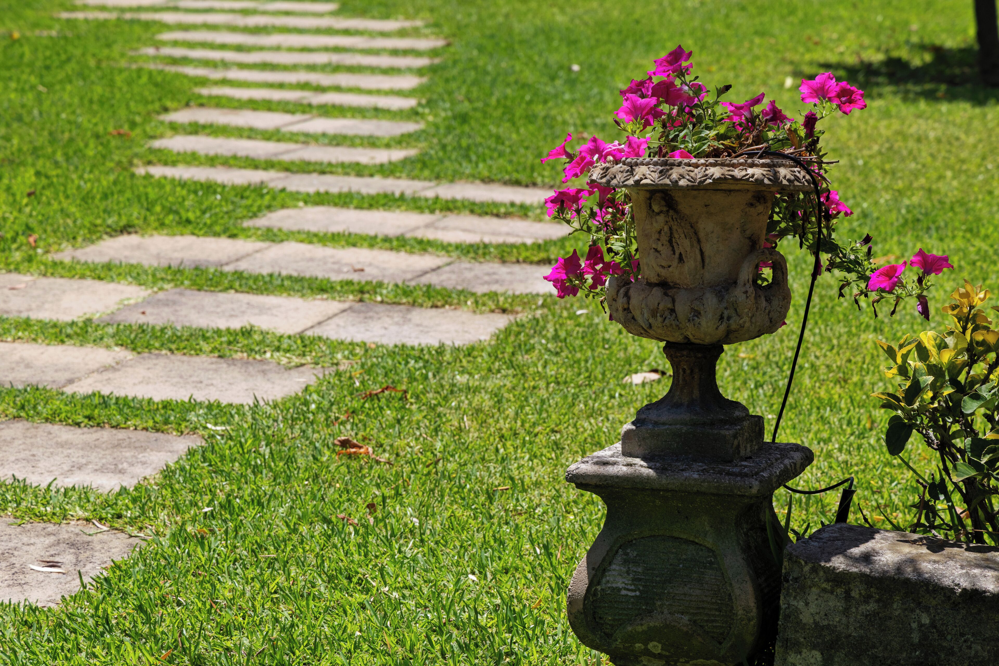 A garden pathway with a stone planter containing pink flowers.