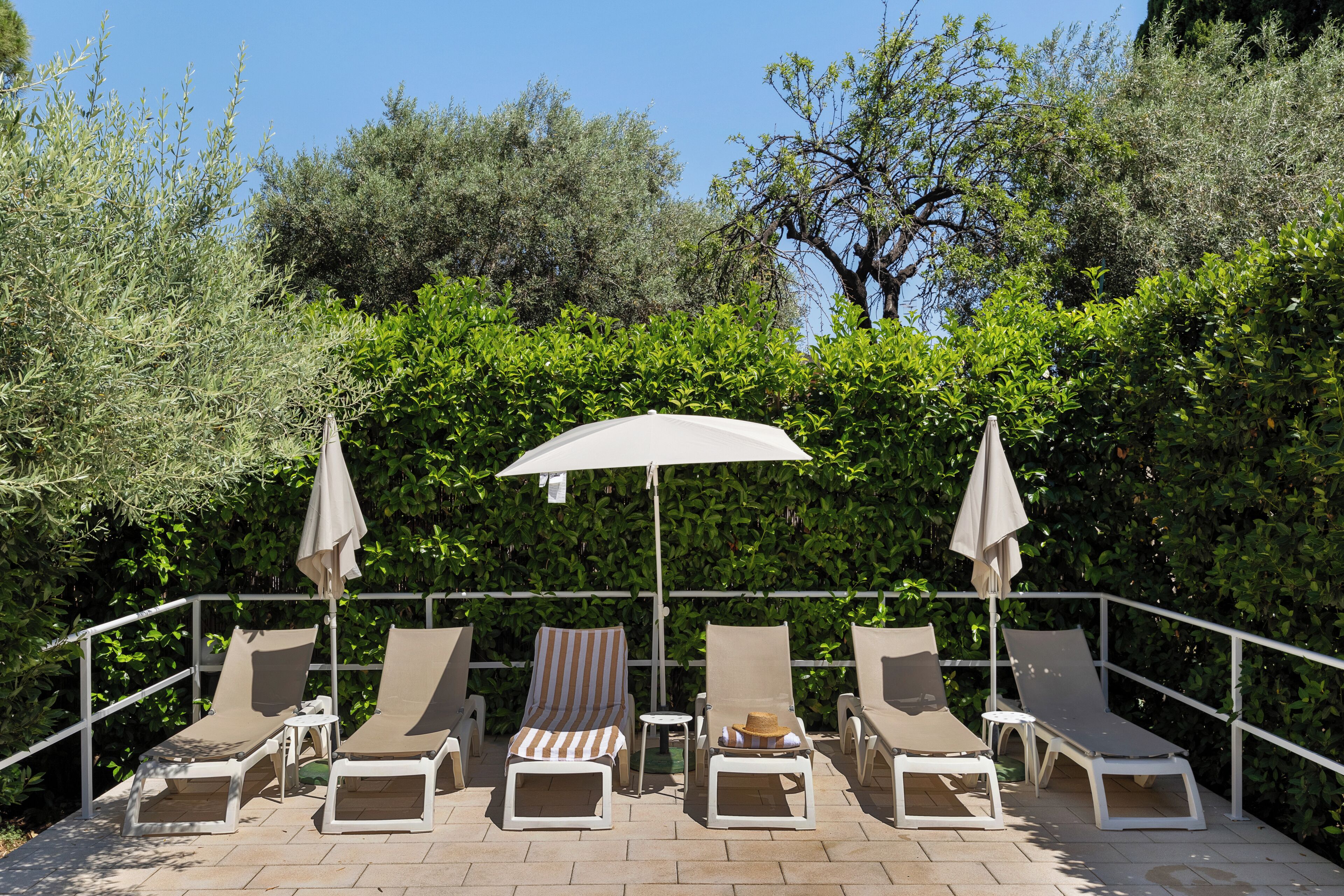 A terrace with lounge chairs and umbrellas, surrounded by greenery.
