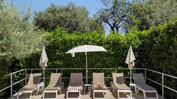 A terrace with lounge chairs and umbrellas, surrounded by greenery.