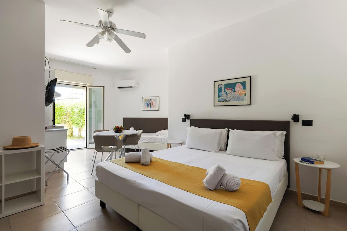 A hotel room with a bed, a desk, a chair, a ceiling fan, and artwork on the walls.