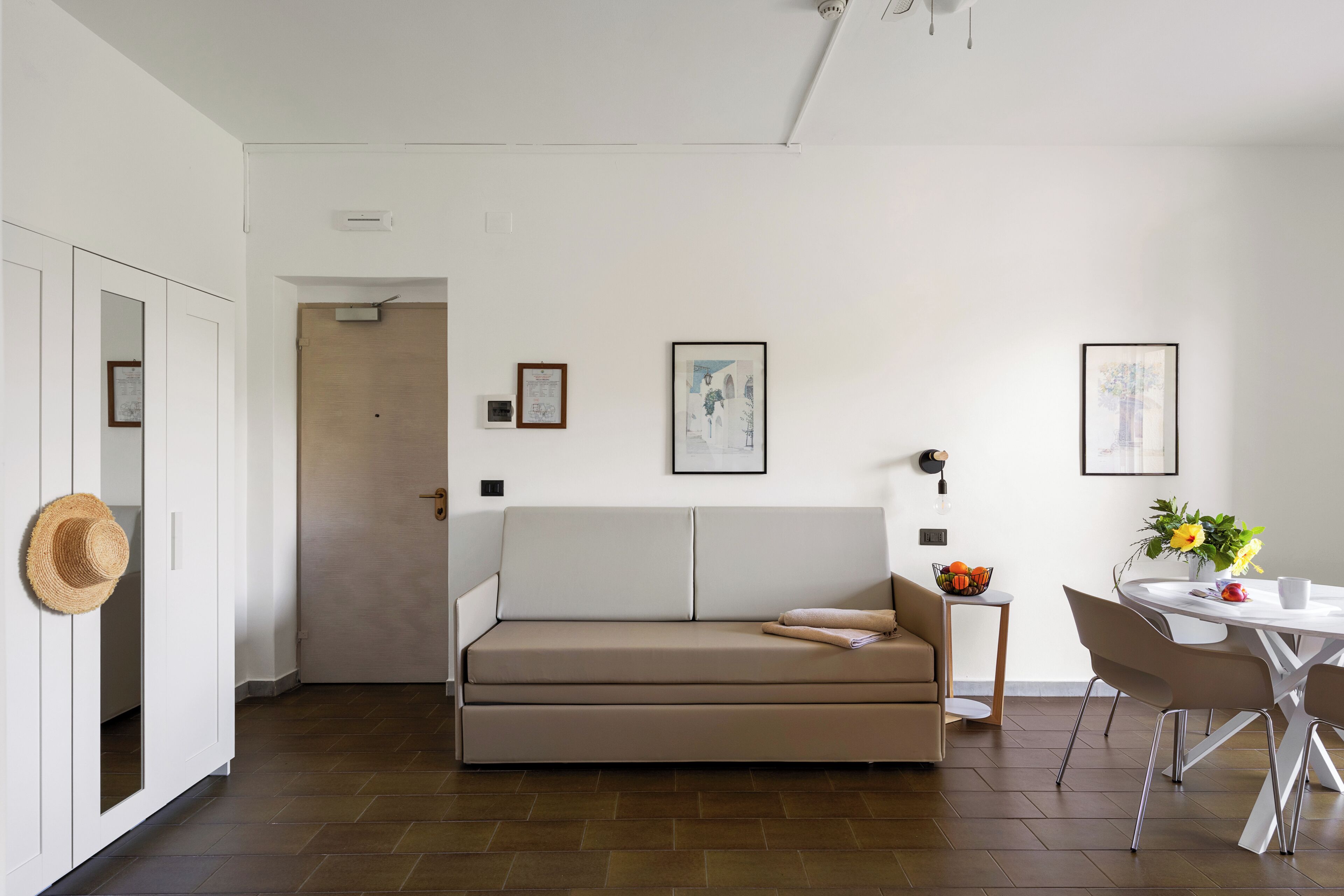 A modern living room with a sofa, a dining table with chairs, and artwork on the walls.