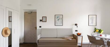 A modern living room with a sofa, a dining table with chairs, and artwork on the walls.