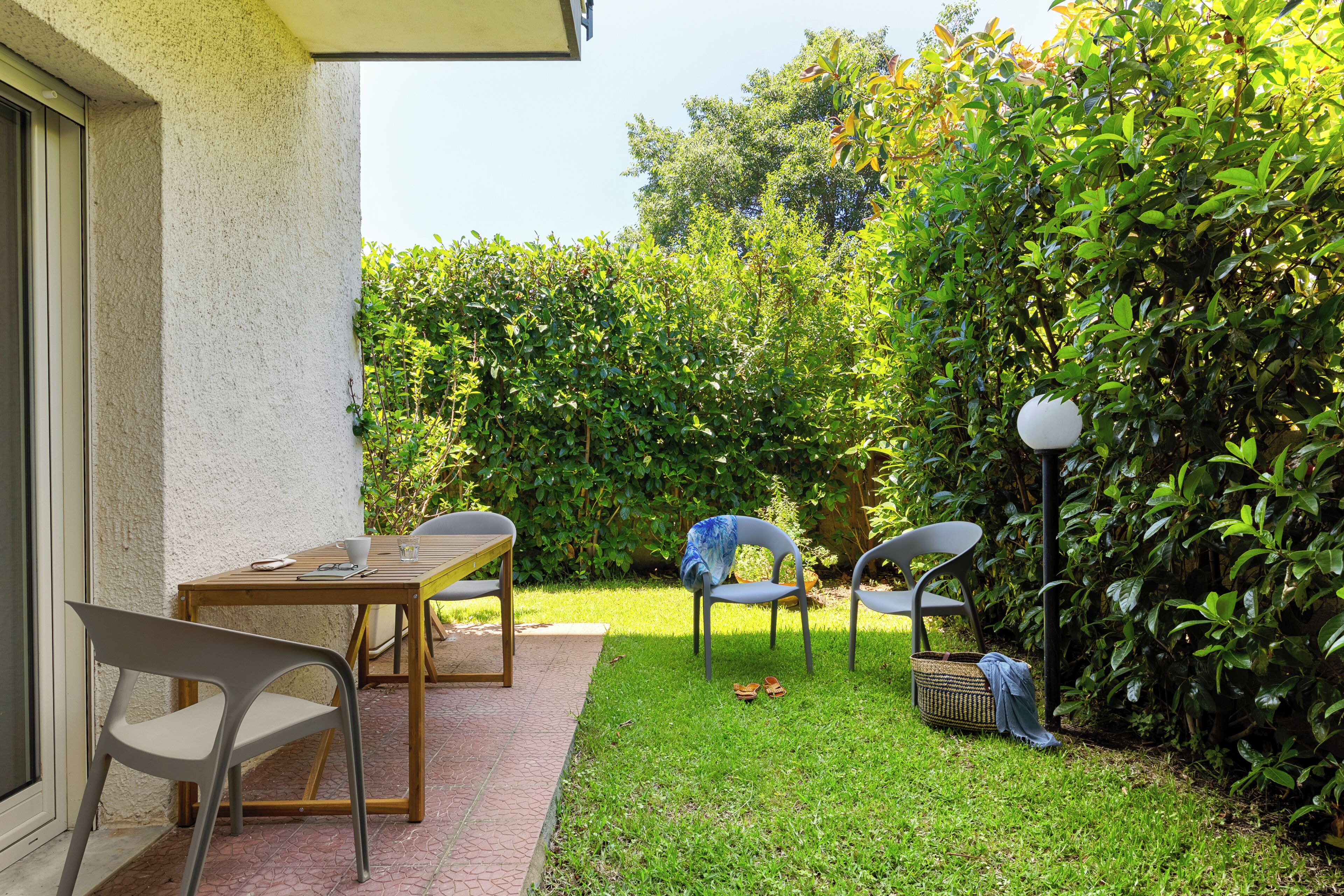 Eine Terrasse mit Tisch und Stühlen, umgeben von Pflanzen und einer Hecke.