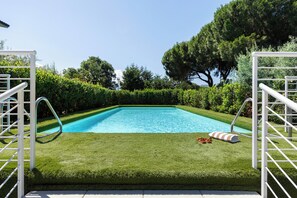 En rektangulär swimmingpool med ett vitt poolområde och metallräcken, omgiven av välskött gräsmatta och häckar.