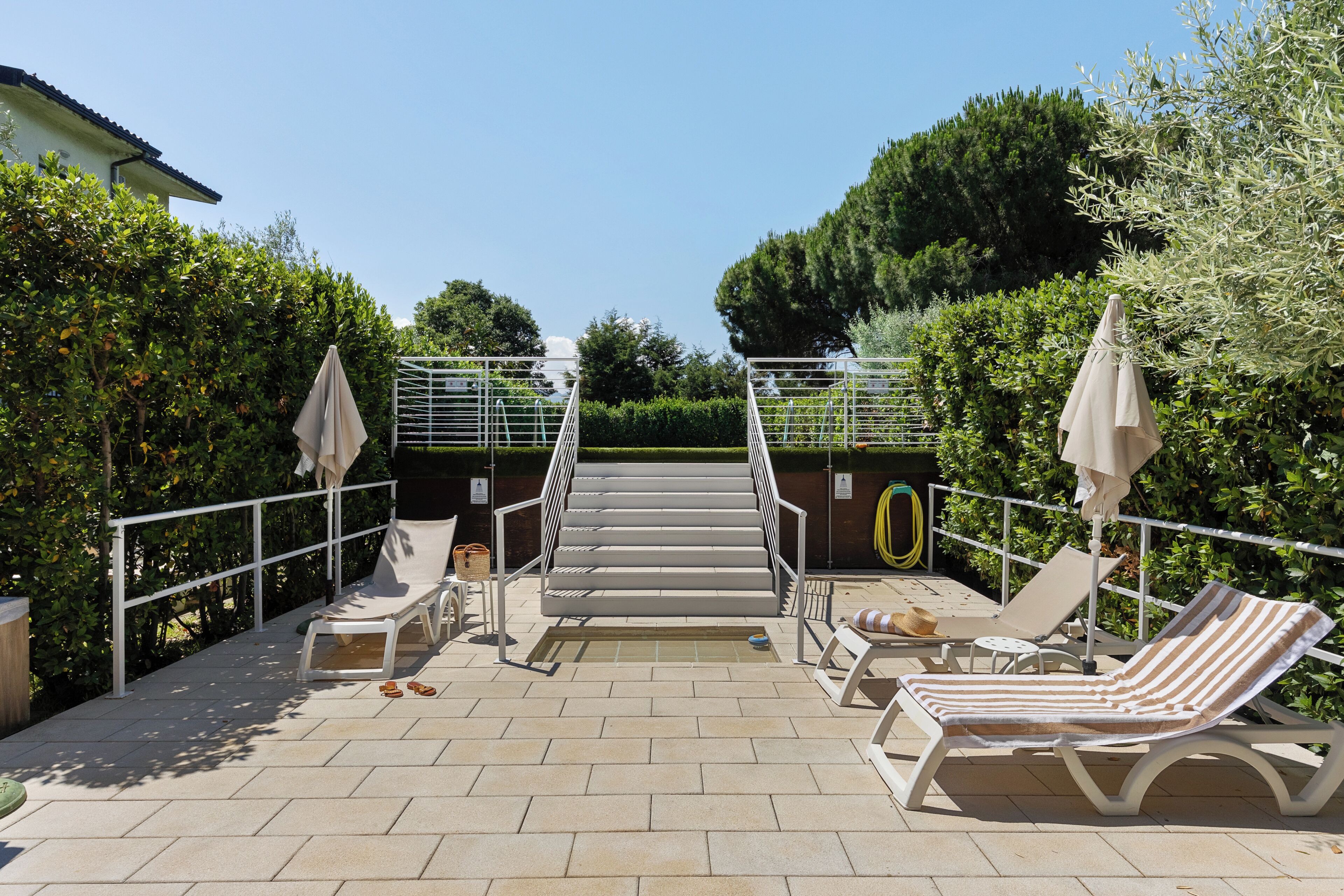 A sunlit outdoor area with a pool, lounge chairs, and a staircase leading to a higher level.
