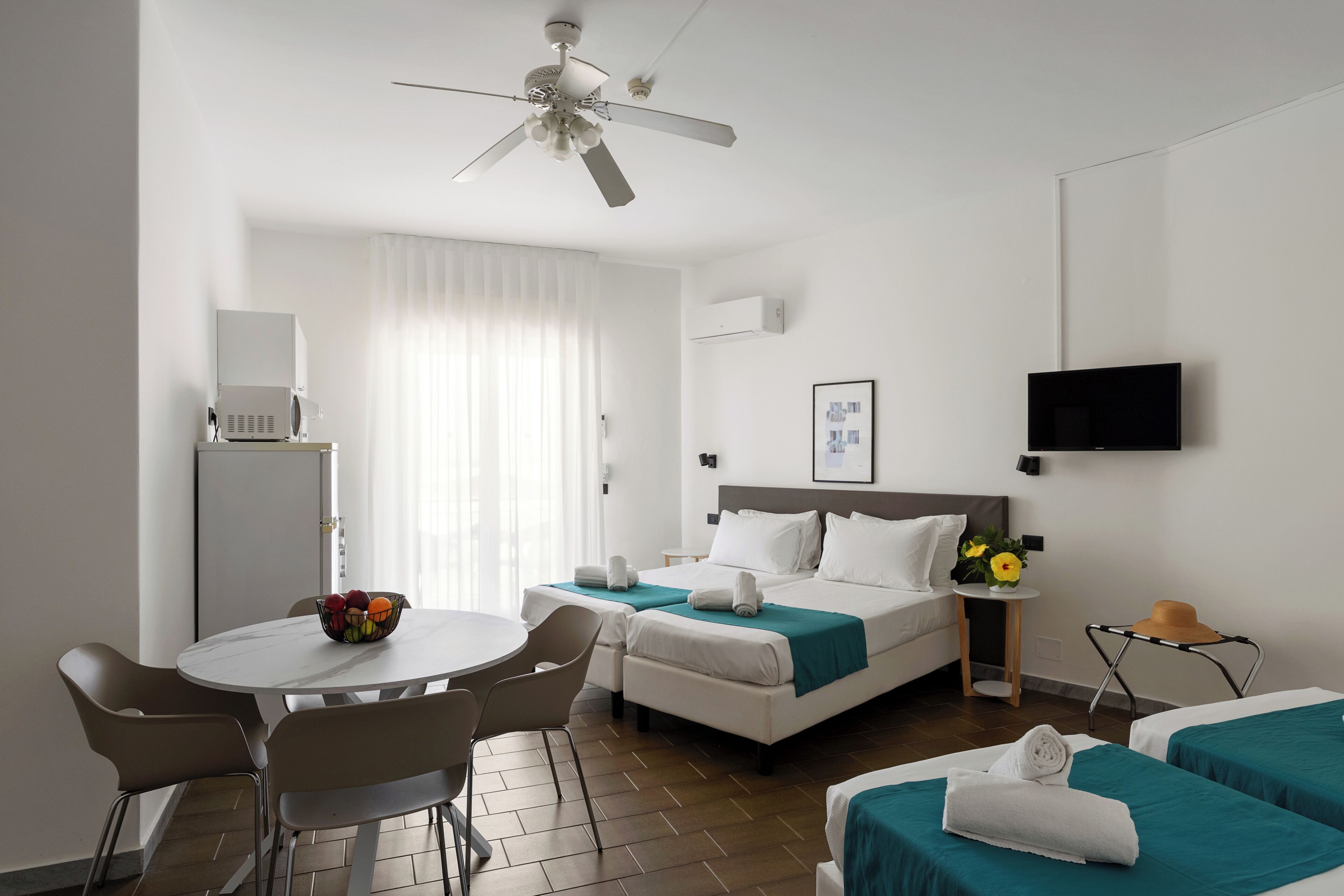Una habitación de hotel con cama, escritorio, silla, televisión y ventilador de techo.