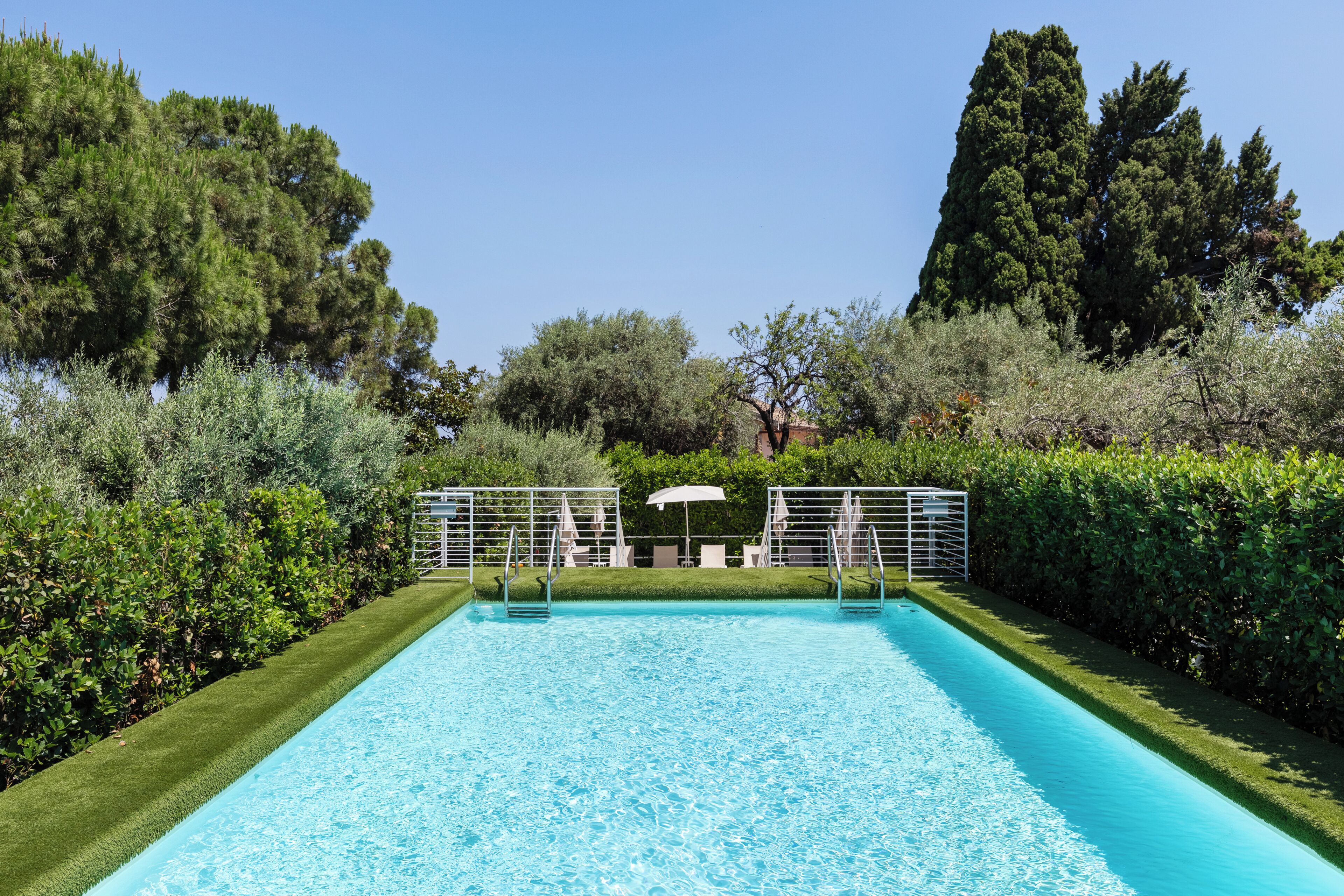 Une piscine rectangulaire à l’eau d’un bleu limpide, entourée de haies et d’arbres bien entretenus.