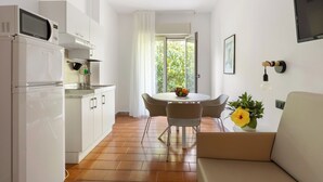 A modern kitchen with a microwave, oven, and sink, a dining area with a table and chairs, and a sofa with a potted plant. - Villa Collina (Giardini Naxos)