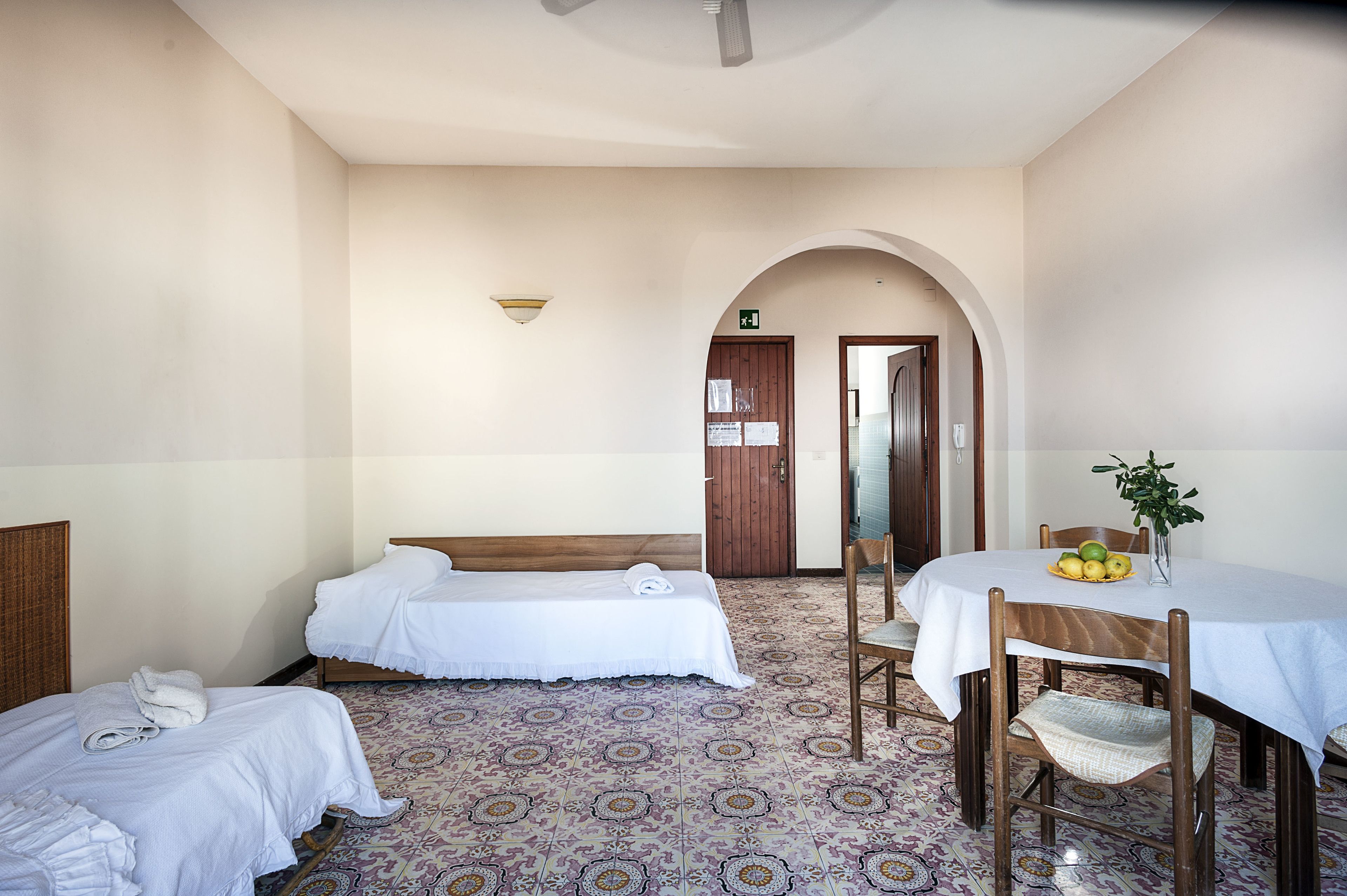 Une chambre d’hôtel avec deux lits simples, une table à manger avec des chaises et une petite table avec une plante.