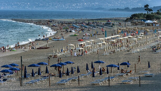 A beach with rows of sun umbrellas and beach chairs, a pier in the background, and the ocean. - Residence Villa Liliana (Giardini Naxos)