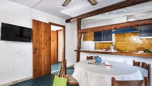 A dining area with a table set for two, a television mounted on the wall, and a wooden door leading to another room. - Residence Villa Liliana (Giardini Naxos)