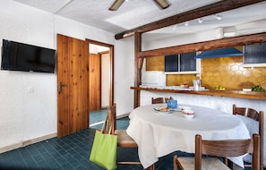 Ein Essbereich mit einem für zwei Personen gedeckten Tisch, einem an der Wand montierten Fernseher und einer Holztür, die in einen anderen Raum führt.
