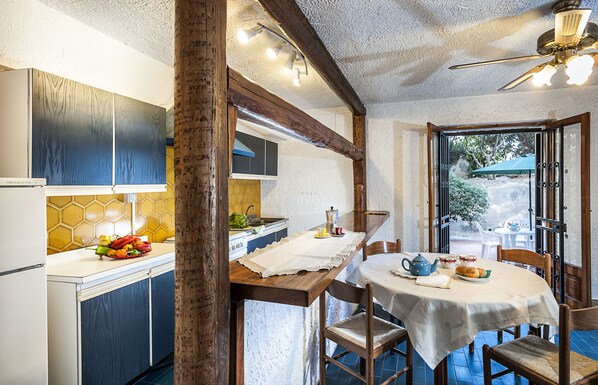 A kitchen with wooden cabinets, a dining table set with a teapot, cups, and a plate of food. - Residence Villa Liliana (Giardini Naxos)