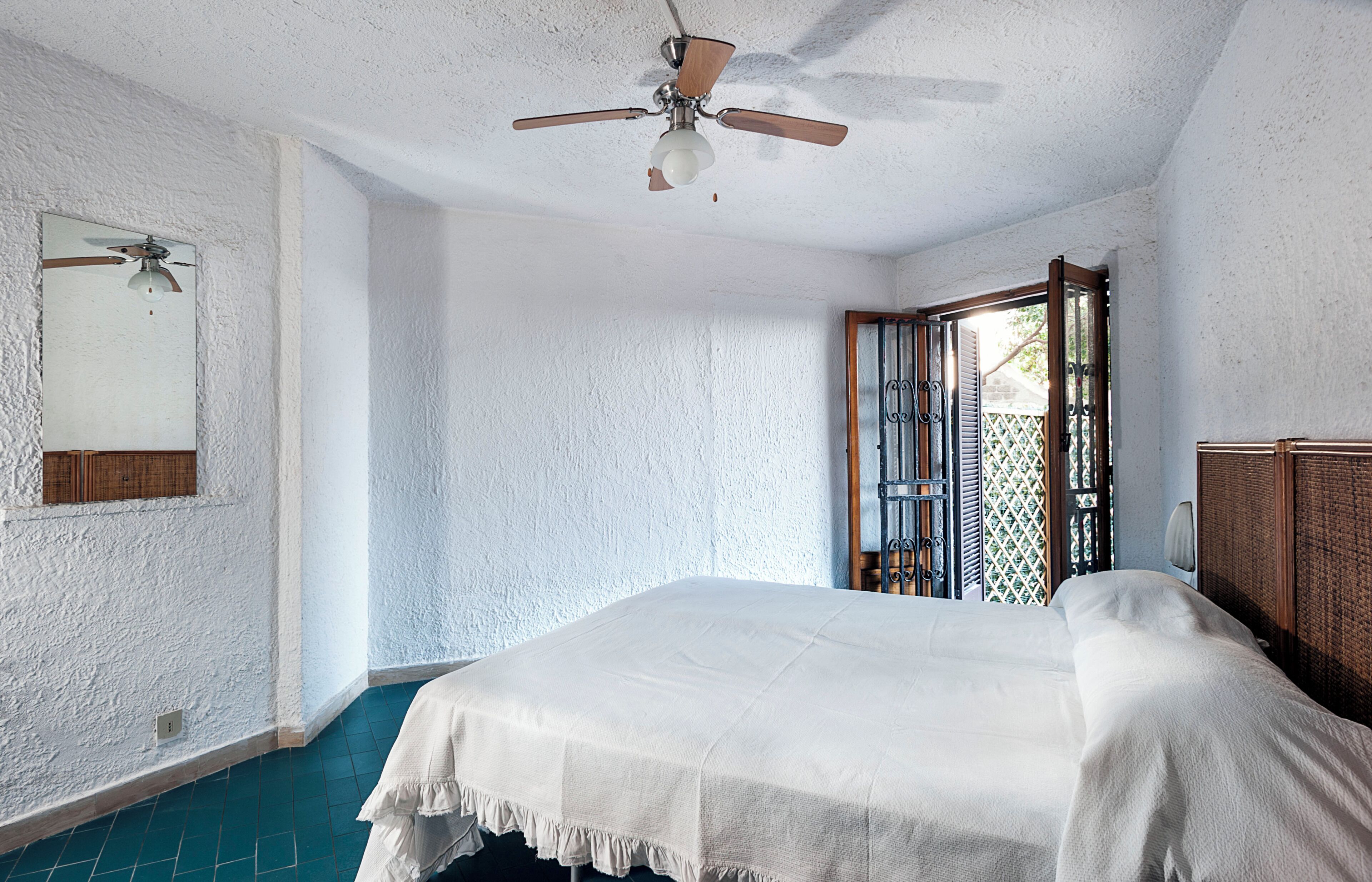Une chambre à coucher avec un lit, un ventilateur de plafond, une fenêtre donnant sur un beau paysage et une porte menant à l’extérieur.