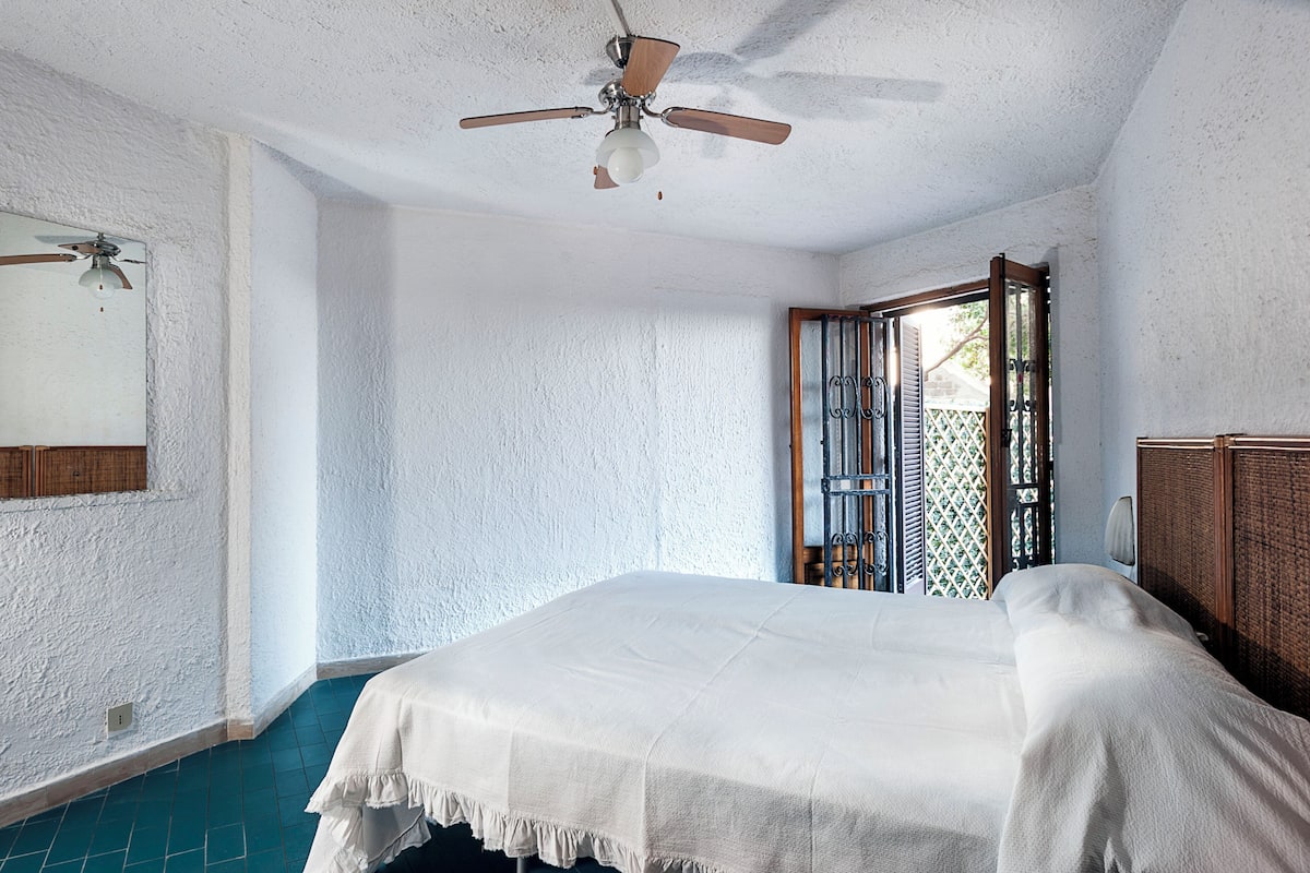 Une chambre à coucher avec un lit, un ventilateur de plafond, une fenêtre donnant sur un beau paysage et une porte menant à l’extérieur.