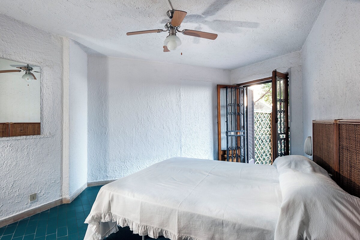 Une chambre à coucher avec un lit, un ventilateur de plafond, une fenêtre donnant sur un beau paysage et une porte menant à l’extérieur.