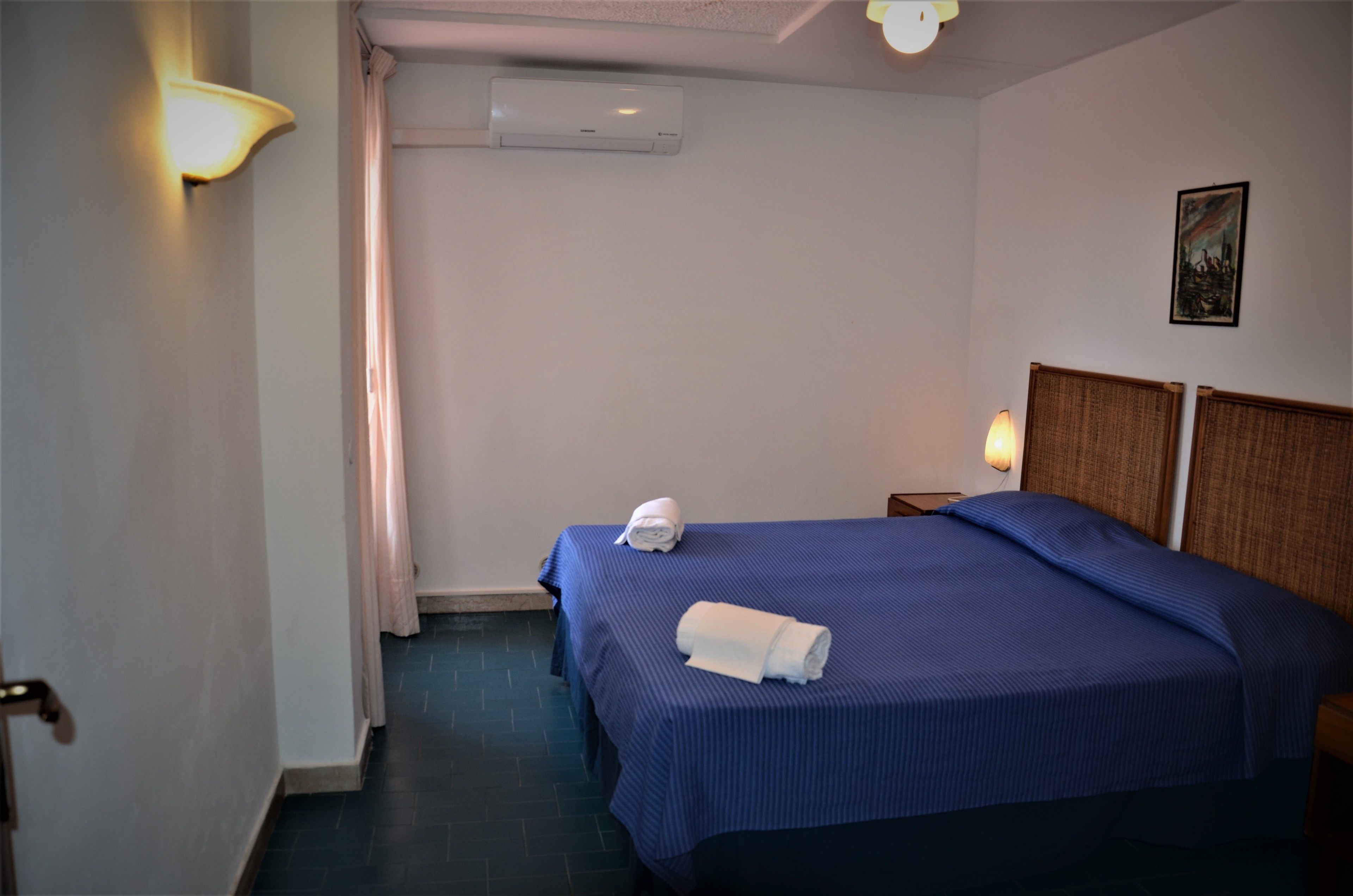Ein Hotelzimmer mit einem Einzelbett, einem Nachttisch, einer Wandaircondition und einem Bild an der Wand.
