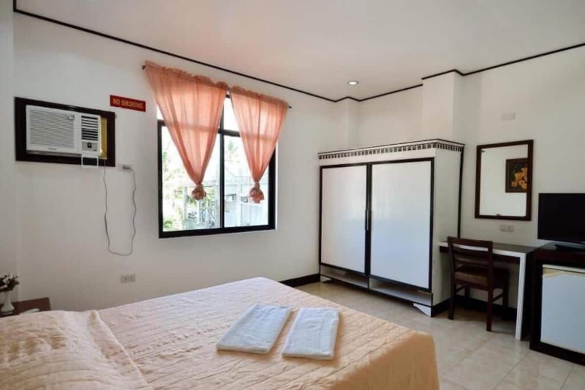 A hotel room with a bed, a desk, a television, a wardrobe, and a window with curtains.