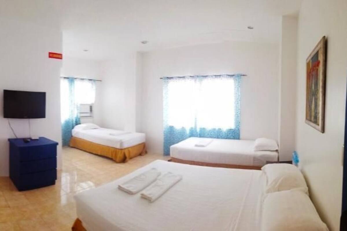 A hotel room with a bed, a TV, a desk, and a window with curtains.