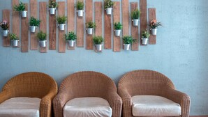 A room with three wicker chairs with cushions, a wall-mounted clock, and a series of wooden panels with potted plants. - Island Inn Boracay (Boracay Island)